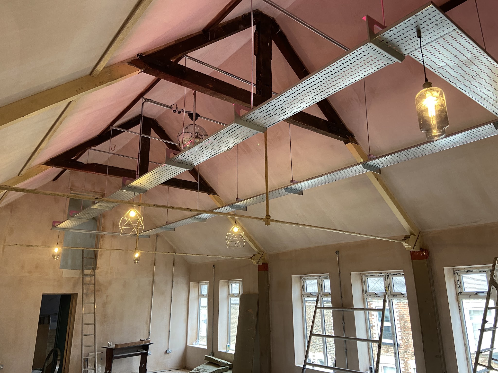 Vaulted room mid-renovation with cable tray across the trusses and filament pendants